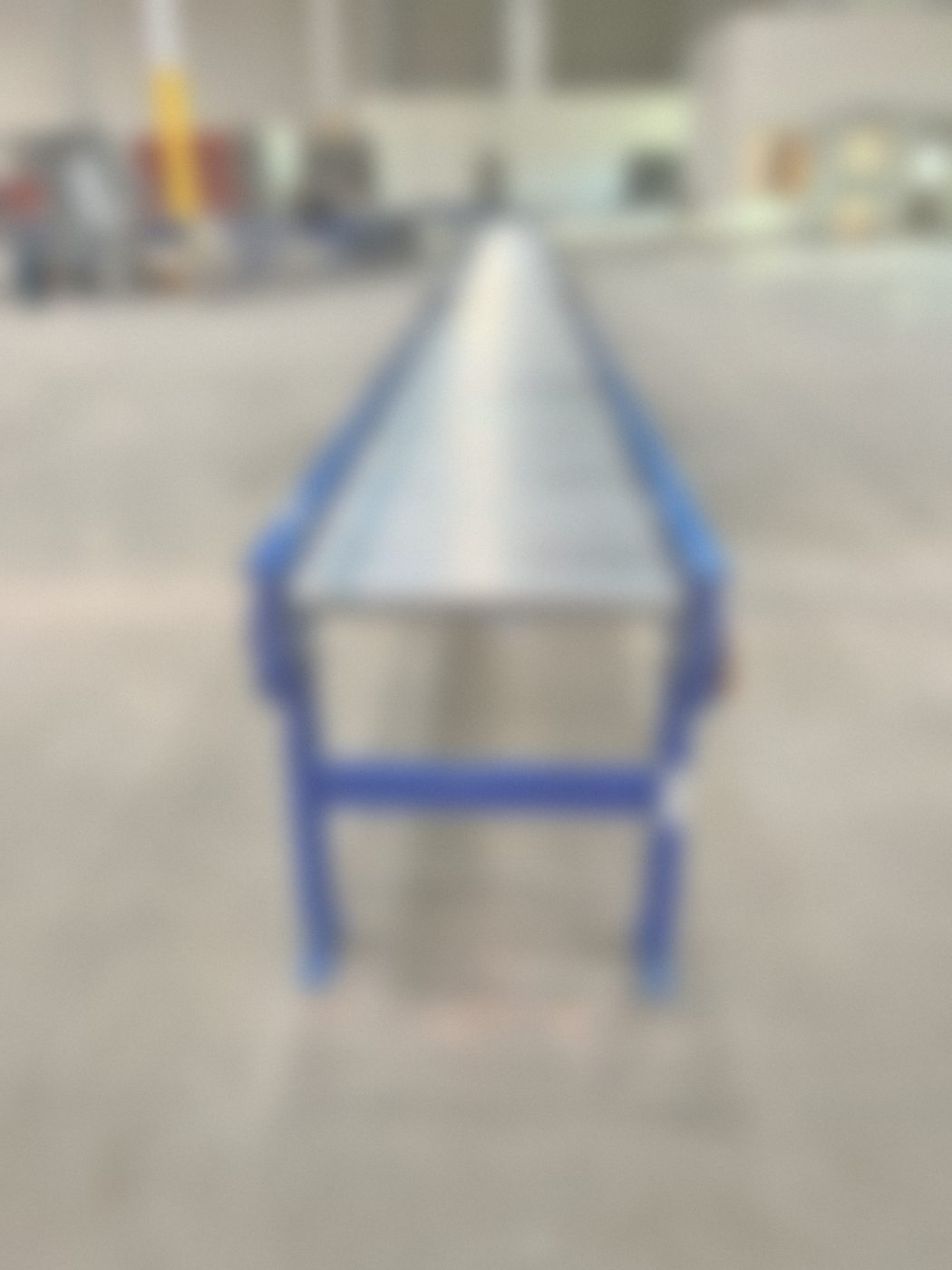 Long roller conveyor on blue stands with control panels in the background