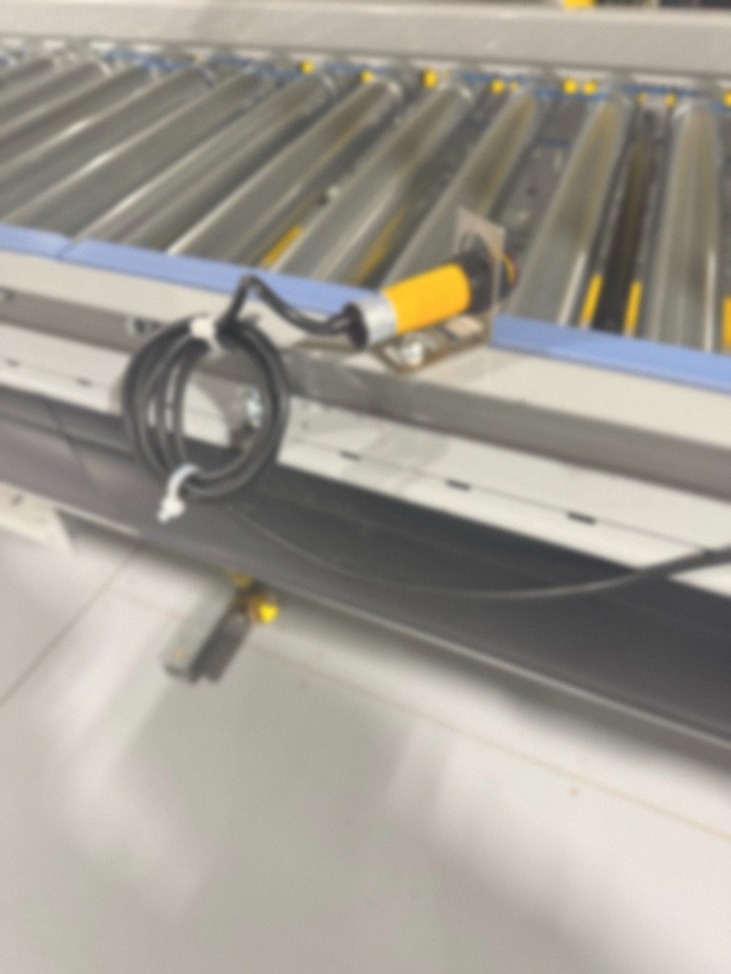 Photoelectric sensor on a proper mounting bracket with its cable secured, on a roller conveyor